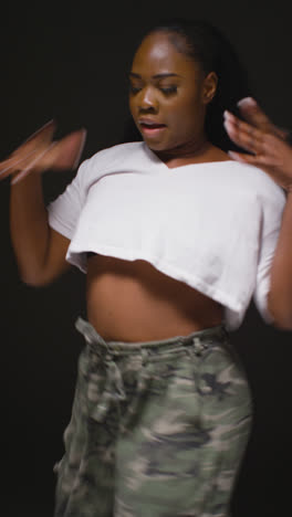 Vertical-Video-Studio-Portrait-Shot-Of-Young-Woman-Dancing-In-Spotlight-Against-Yellow-Background-2